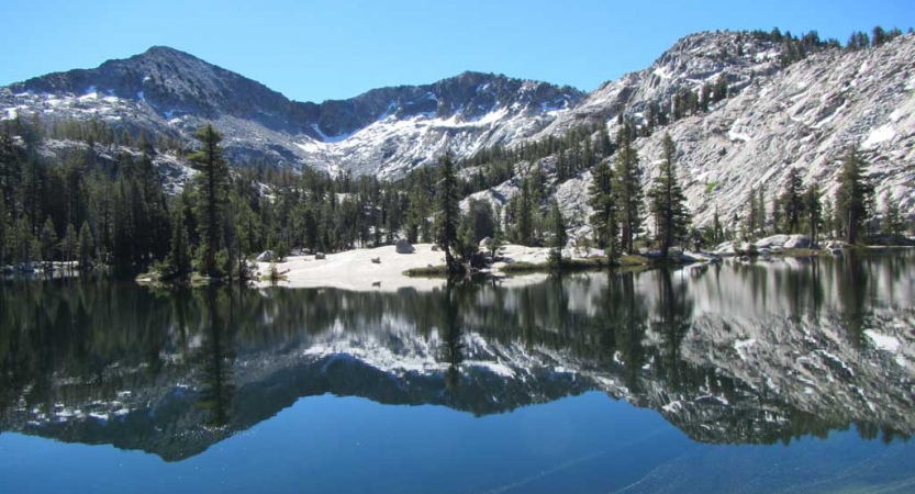 An alpine lake reflects the snow covered mountain nestled beside it. 